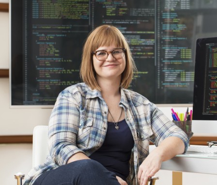 Person smiling at desktop computer with code on screen