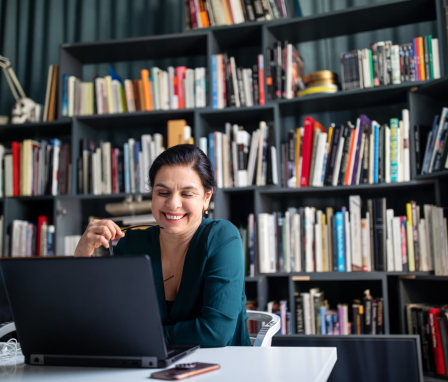 Woman on laptop with bookshelf in background