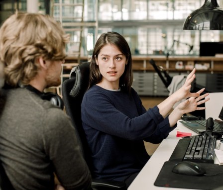 Two people talking while sitting at computers