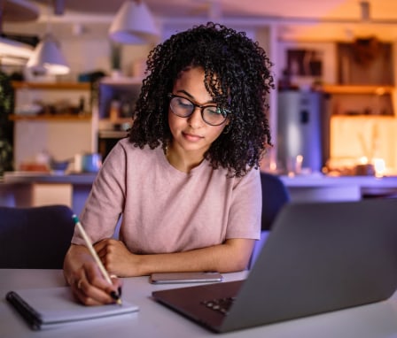 Young student girl learning for exam late at night at her home, using laptop.