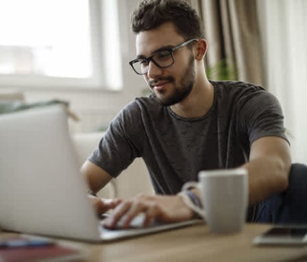 Man working on his laptop with a cup of coffee next to him on his desk