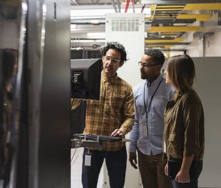 Three colleagues working on computer together in server room