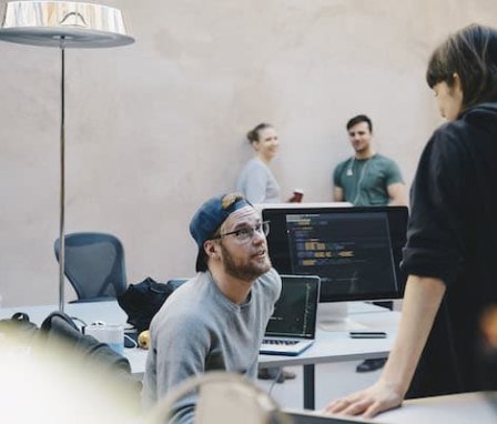 Colleagues talking in office with computers showing code