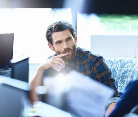 Two men talking while sitting at computer desks