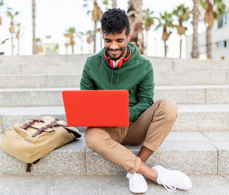 Student sitting outside on stairs and typing on laptop