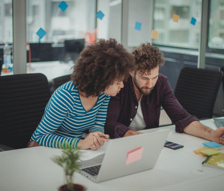 Two people looking at a smart phone in an office with laptops